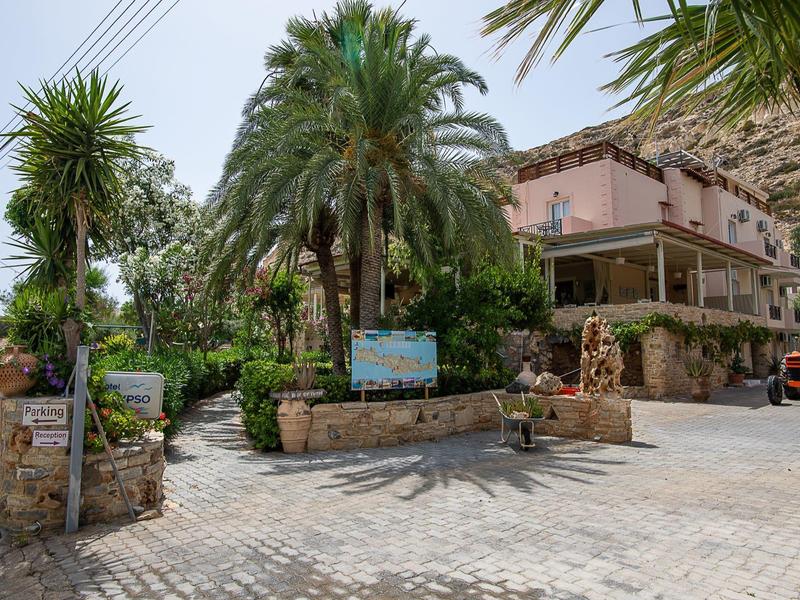 Small hotel surrounded by palm trees with paved parking and entrance.