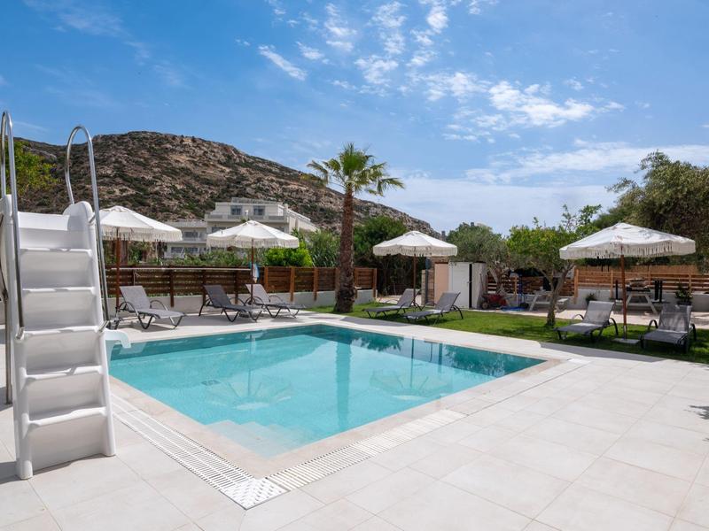 Swimming pool with slide, sun umbrellas, and loungers in front of rocky hill under blue sky.