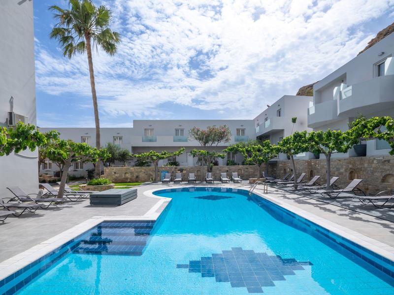 A clear blue pool surrounded by lounge chairs and white buildings under a cloudy sky.