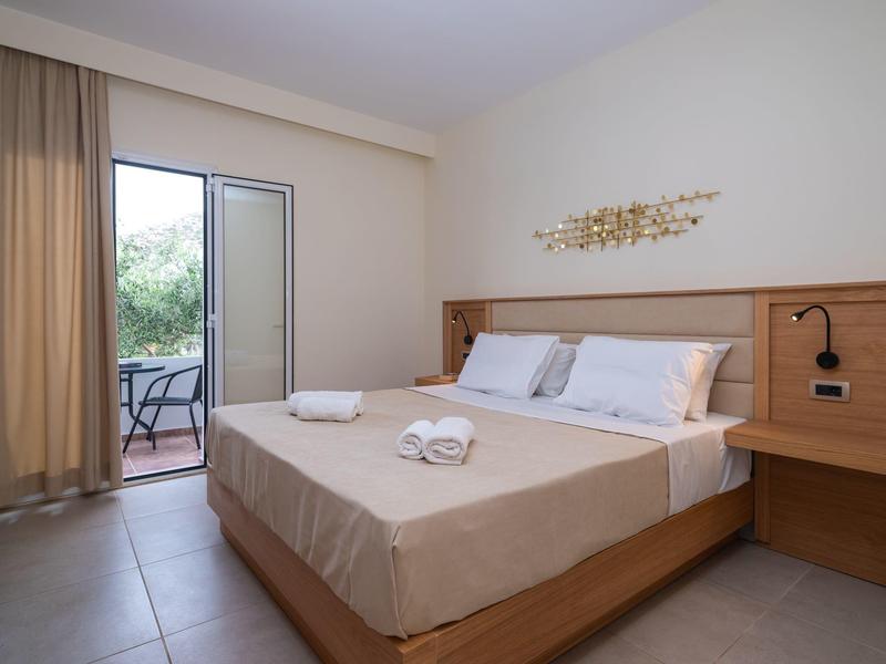 Bright bedroom with double bed, towels, and balcony overlooking garden.