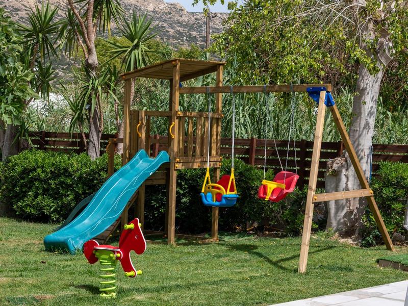 A wooden playground with a blue slide, swing set, and a red rocking horse on grass.