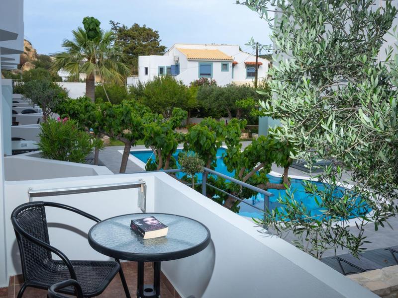 Balcony with round glass table, chairs, and view of pool and white houses.