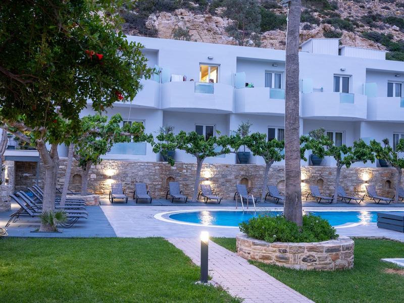 Modern white hotel complex with pool, palm trees, and illuminated surroundings at dusk.