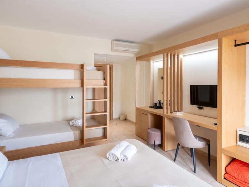 Hotel room with bunk bed, double bed, workspace, and TV in a bright design.