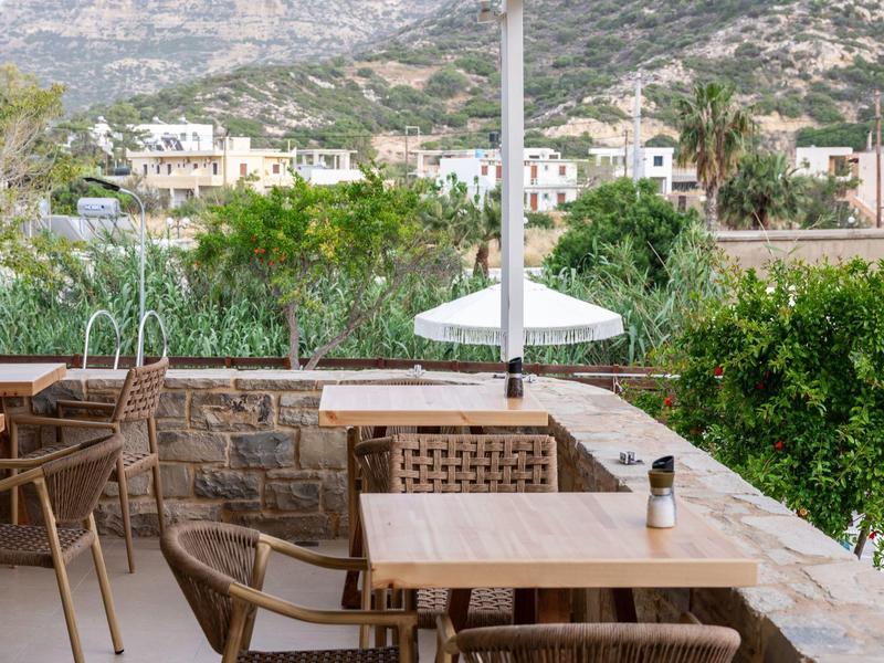Sunny terrace with wooden chairs and tables, green landscape and mountains in the background.