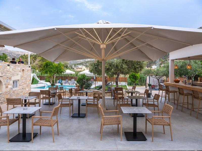 Outdoor café with wooden chairs and tables under large white umbrellas on a clear day.