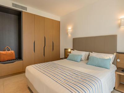 Lichte hotelkamer met groot tweepersoonsbed, beige muur en bruine kasten.