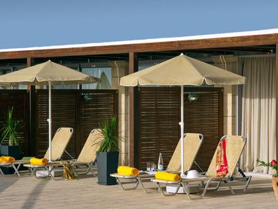 Drie ligstoelen onder parasols voor houten panelen bij een hotel met planten.