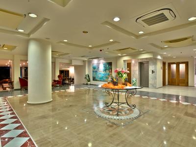 Bright hotel lobby with marble floor, columns, and a round table with flower arrangement.
