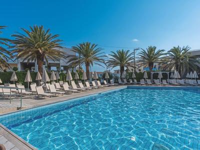 Groot buitenzwembad met ligstoelen en palmbomen onder een blauwe lucht bij een hotelresort.