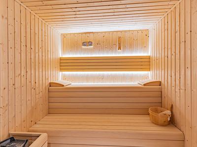 Lichte houten sauna met banken, emmer en sfeerverlichting op de achterwand.