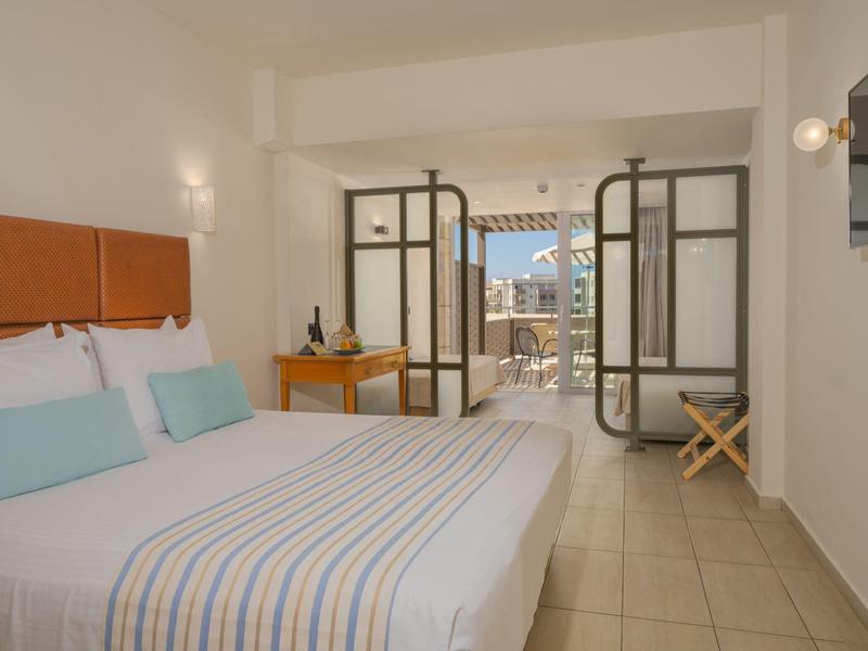 Lichte hotelkamer met groot bed, bureau en balkon met uitzicht op landschap.