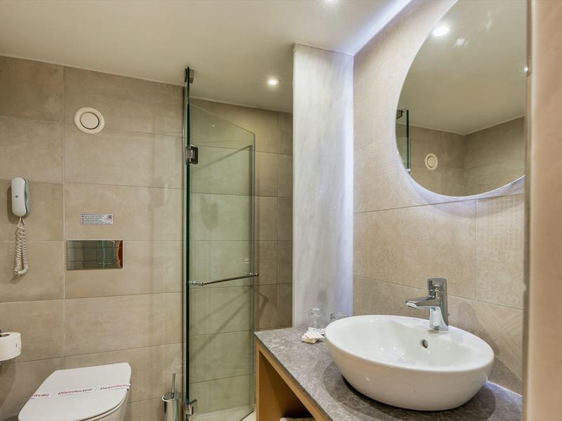 Modern badkamer met ronde spiegel, glazen douche en witte wastafel.