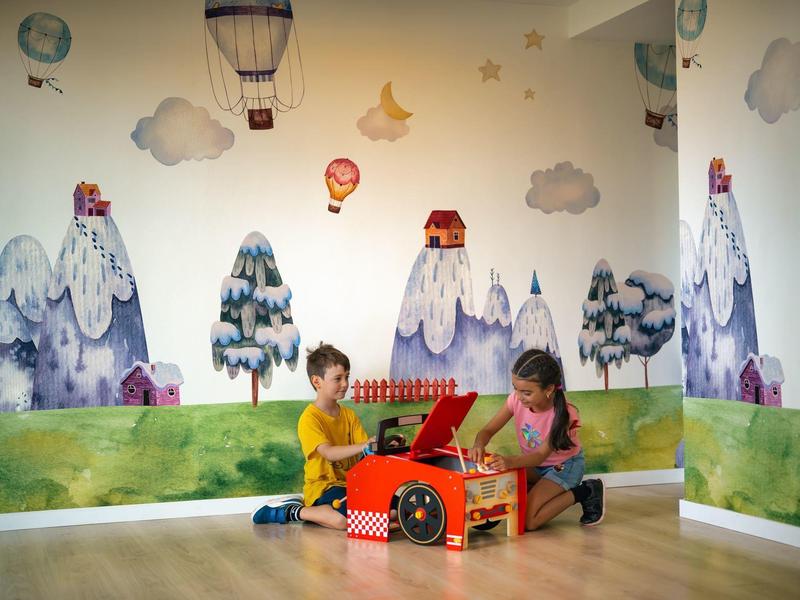 Kinderen spelen op houten vloer voor een muur met bergen en luchtballon muurschilderingen.