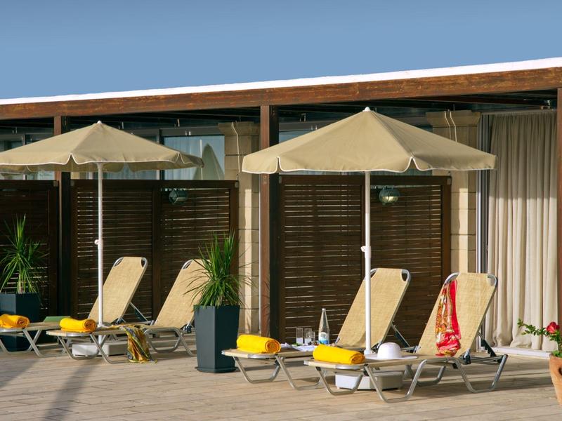Drie ligstoelen onder parasols voor houten panelen bij een hotel met planten.