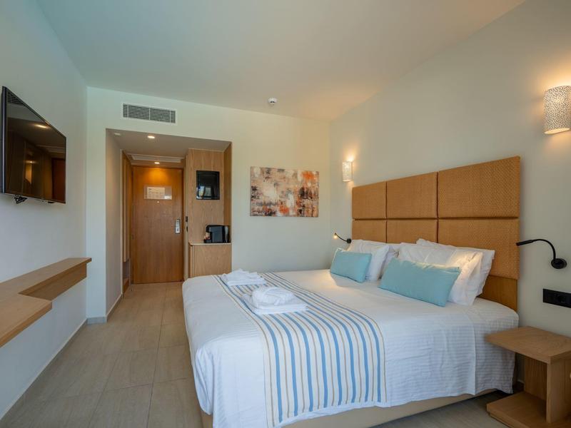 Lichte hotelkamer met tweepersoonsbed, moderne meubels en tv aan de muur.