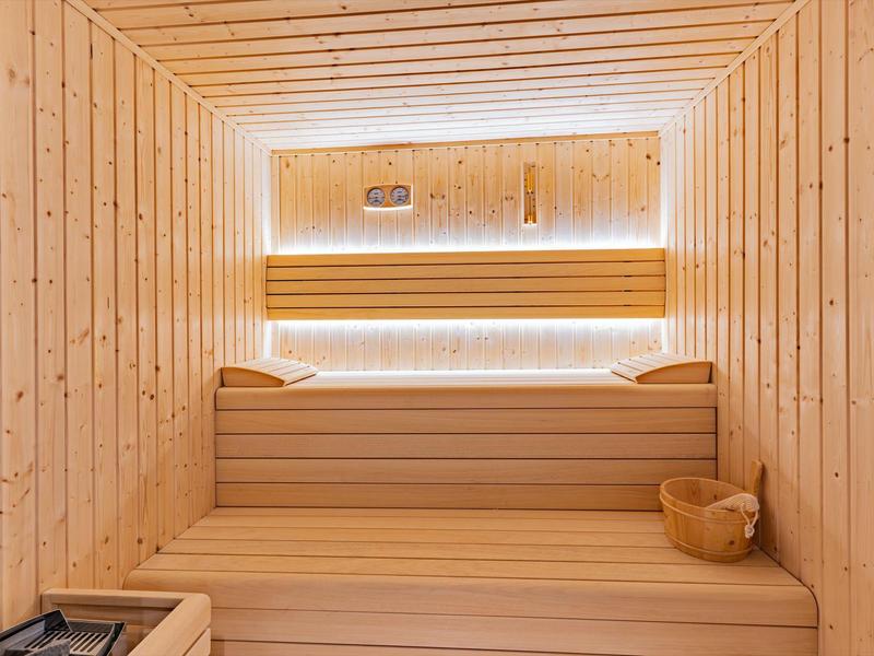 Lichte houten sauna met banken, emmer en sfeerverlichting op de achterwand.