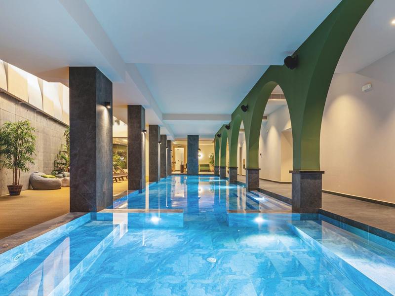Overdekt zwembad met blauw water, pilaren en groene bogen in een modern hotel.