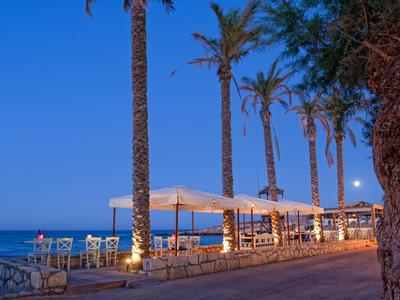 Passeggiata sul mare con palme, aree salotto illuminate e vista sul mare al crepuscolo.