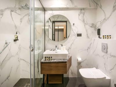 Bagno moderno con piastrelle in marmo, doccia in vetro, specchio ovale, lavabo e WC.