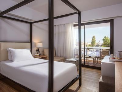 Camera singola con letto a baldacchino, scrivania, lampada e balcone con vista su alberi e acqua.