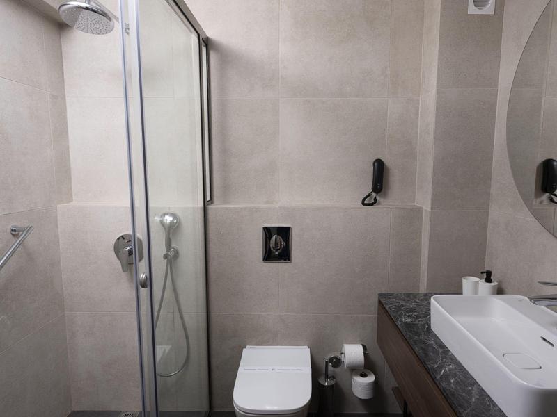 Bagno moderno con doccia, WC e lavabo su piastrelle grigie.