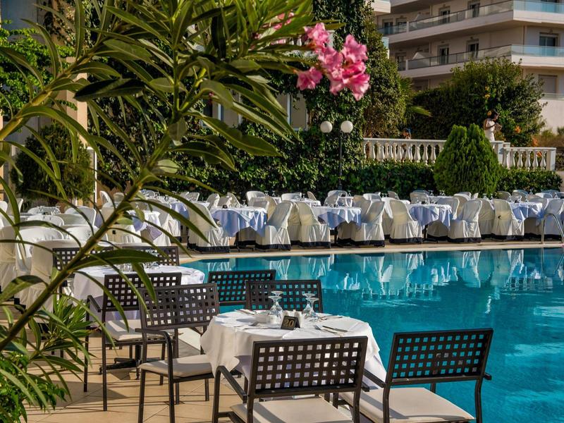 Piscina all'aperto con tavoli apparecchiati e sedie in un giardino d'hotel.