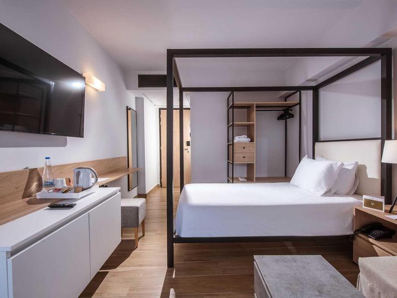 Camera d'albergo moderna con letto a baldacchino, TV, minibar e decorazioni in legno caldo.