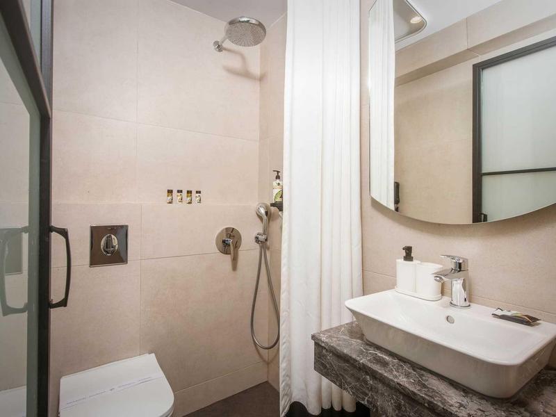 Bagno moderno con doccia a filo, lavabo e grande specchio rotondo.