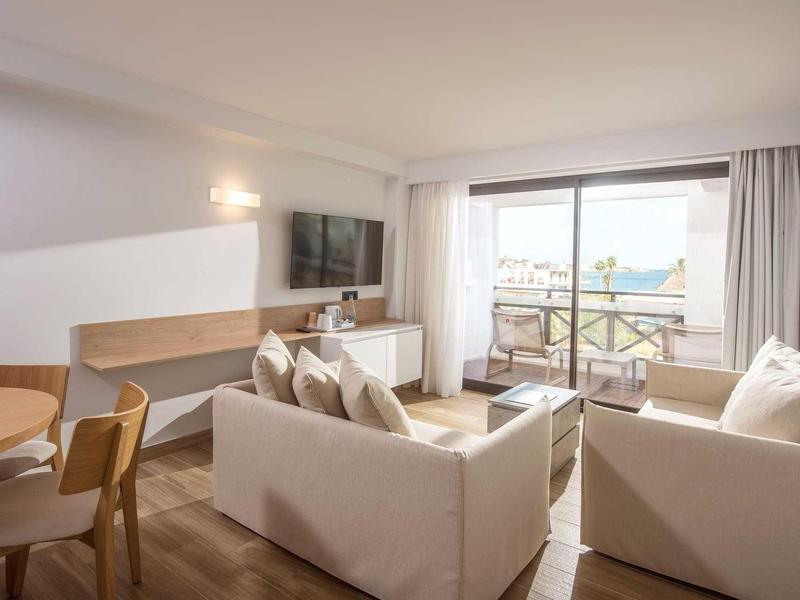 Soggiorno moderno con divani bianchi, TV e balcone con vista sul mare.