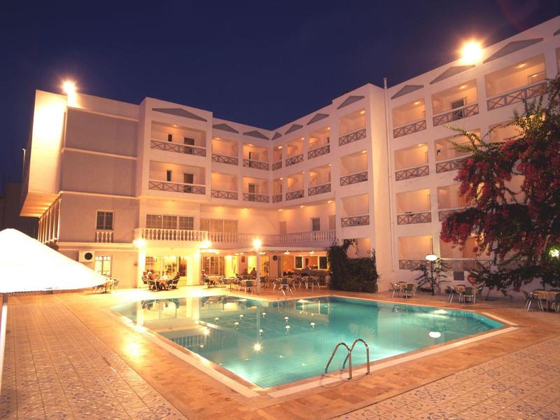 Una piscina dell'hotel illuminata di notte con edificio multipiano adiacente e alberi.