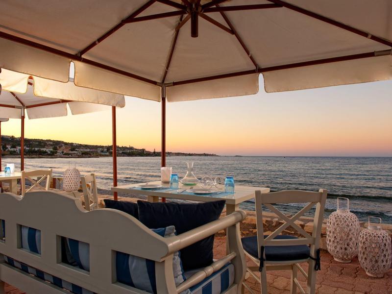 Terrazza di ristorante con posti a sedere e vista sul mare al tramonto.