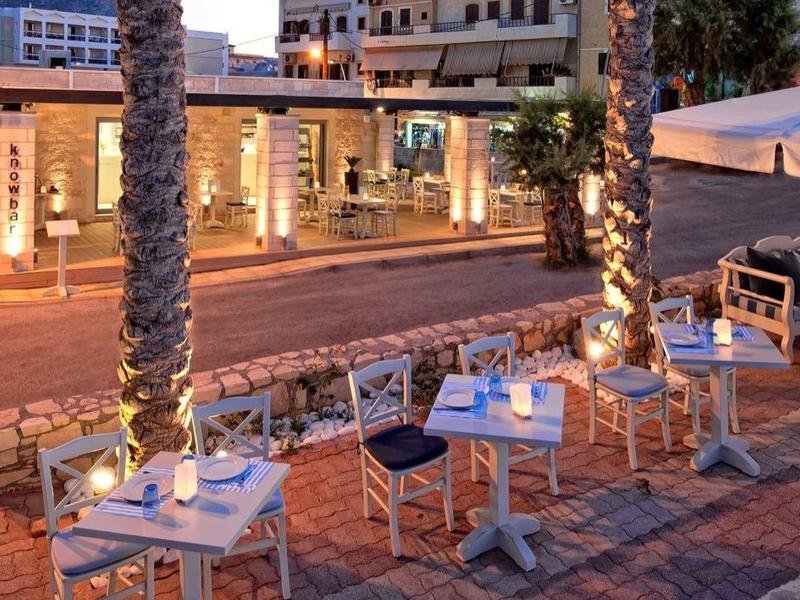 Ristorante all'aperto con tavoli apparecchiati e sedie bianche accanto a una strada di sera