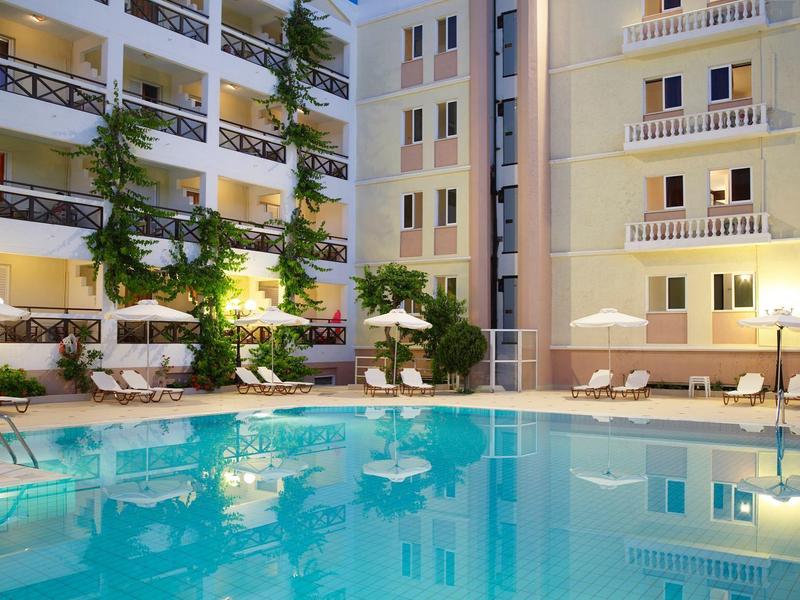 Piscina dell'hotel illuminata di notte con sdraio e edifici moderni sullo sfondo.