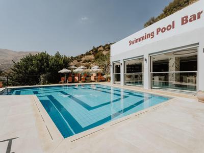 Moderní bazén s čistou modrou vodou a přilehlým barem v slunném resortu.