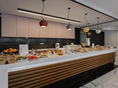 Buffet mit verschiedenen Speisen und Backwaren in modern eingerichteter Frühstückslounge.