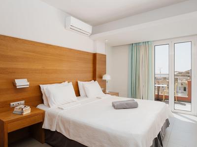 Moderní hotelový pokoj s manželskou postelí, dřevěným čelem postele, klimatizací a balkonem s výhledem na město.