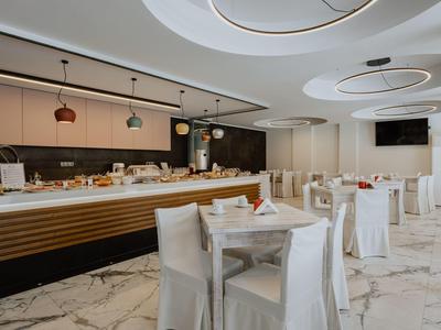 Moderní hotelová restaurace s bílými ubrusy na stolech a bufetovou stanicí v pozadí