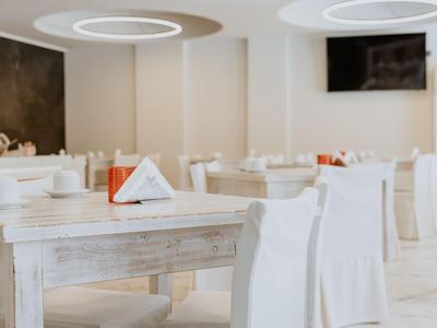 Helles, modern eingerichtetes Restaurant mit weißen Tischen und Stühlen sowie runden Deckenleuchten.