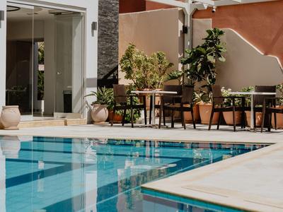 Moderní venkovní bazén s modrými dlaždicemi a posezením s stolem a rostlinami.