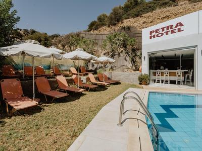 Pool mit blauer Wasserfläche neben Sonnenliegen und weißen Sonnenschirmen vor Hostelgebäude im sonnigen Gelände