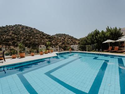 Freier Außenpool mit Liegestühlen und Bergen im Hintergrund an einem sonnigen Tag.