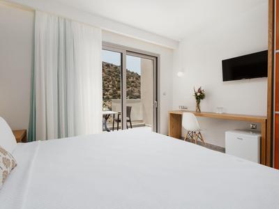 Světý hotelový pokoj s manželskou postelí, psacím stolem, televizí a přístupem na balkon.