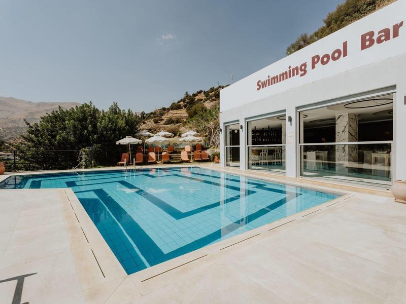 Moderní bazén s čistou modrou vodou a přilehlým barem v slunném resortu.