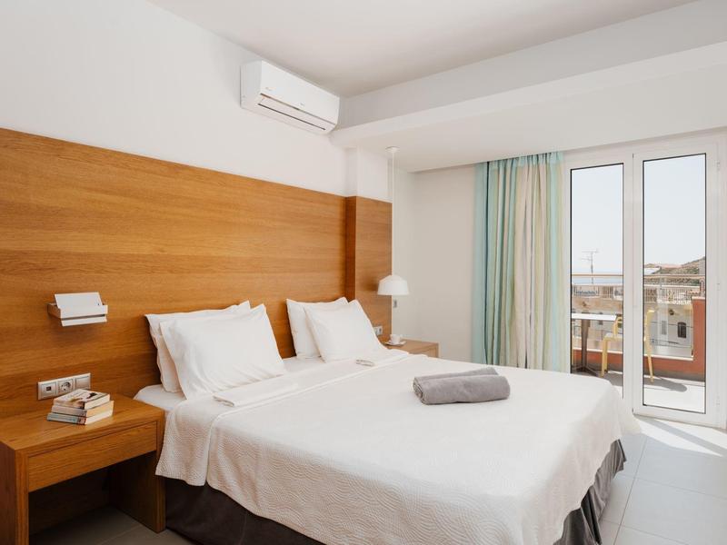 Moderní hotelový pokoj s manželskou postelí, dřevěným čelem postele, klimatizací a balkonem s výhledem na město.