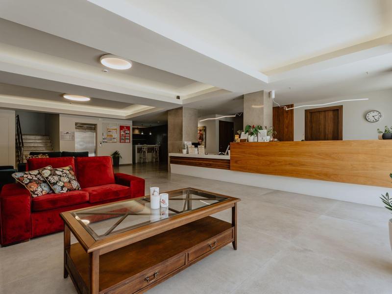 Moderní hotelová hala s červenou pohovkou, dřevěným stolem a světlou recepcí.