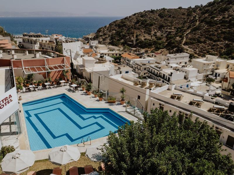 Pohled na hotelový bazén s modrými vodními pruhy v městě na kopci s mořem v pozadí.