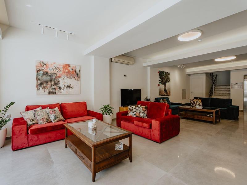 Moderní obývací pokoj s červenými pohovkami, dřevěným stolem a dekoracemi v světlém hotelovém pokoji.