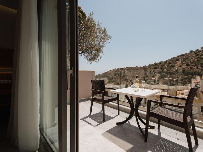 Balkon s stolem a židlemi s výhledem na kopcovitou krajinu pod jasnou oblohou.