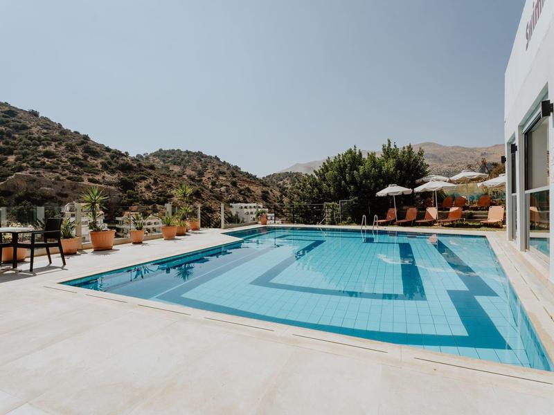 Moderní bazén s pohodlným posezením a kopci v pozadí pod jasnou oblohou.